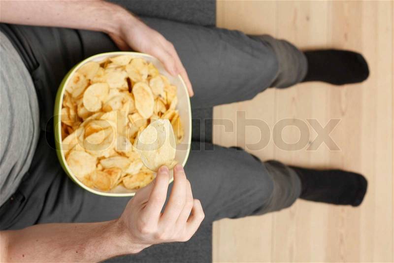 A bowl of chips in the lap of a man sitting on a chair, stock photo