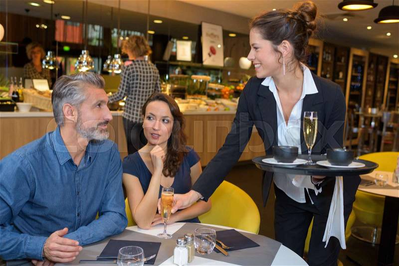 Waitress serving drinks to couple in restaurant, stock photo