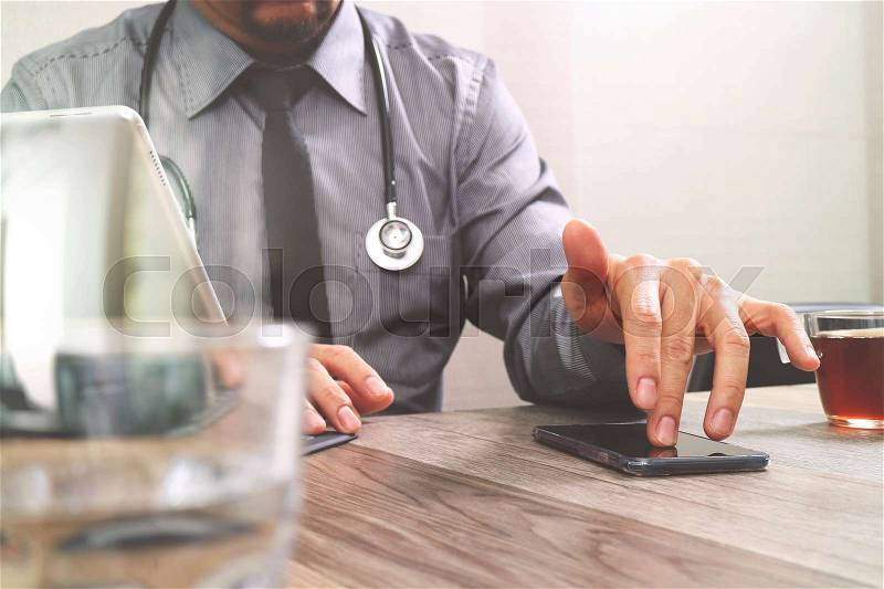 Smart medical doctor hand working with smart phone,digital tablet computer,stethoscope eyeglass,on wood desk,filter effect, stock photo