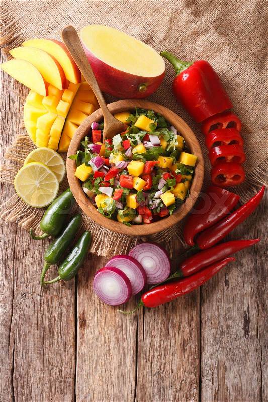Mexican Food: salsa with mango, cilantro, onions and peppers close up in a bowl and ingredients on the table. vertical view from above\, stock photo