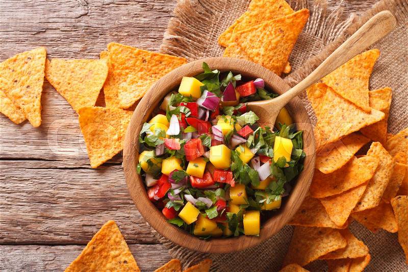 Mexican salsa with mangoes, peppers, cilantro and onion close up in a bowl and corn chips on the table. Horizontal view from above , stock photo