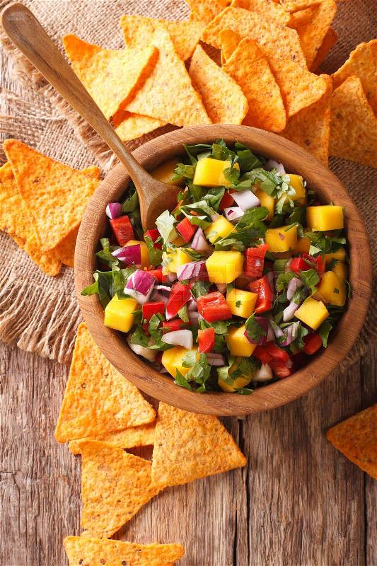Mexican salsa with mangoes, peppers, cilantro and onion close up in a bowl and corn chips on the table. vertical view from above\, stock photo