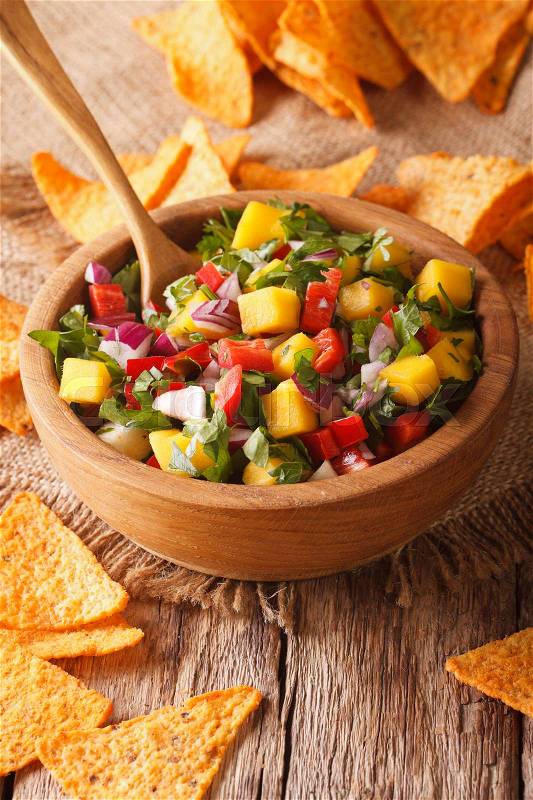 Mexican Food: salsa with mangoes, peppers, cilantro and onion close up in a bowl and nachos on the table. vertical\, stock photo