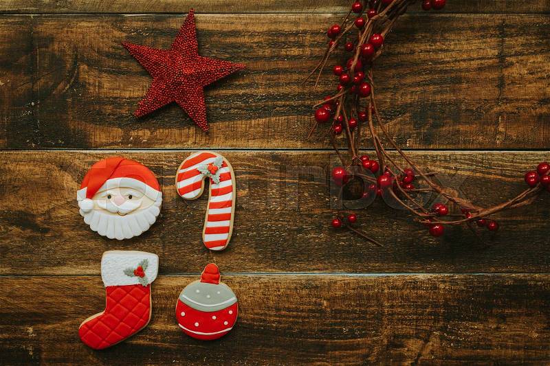 Red cookies for Christmas and a branch with red berries on a wooden background, stock photo