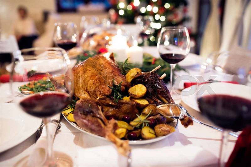 Christmas meal laid on table in decorated dining room. Roasted turkey or chicken, vegetables, Christmas wreath, glass of red wine, stock photo