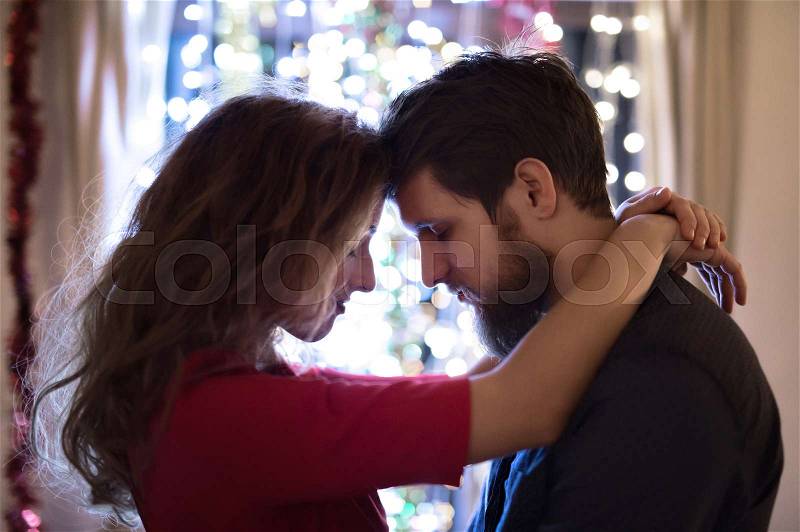 Beautiful hipster couple celebrating the end of the year, having party on New Years Eve, chain of lights behind them, stock photo