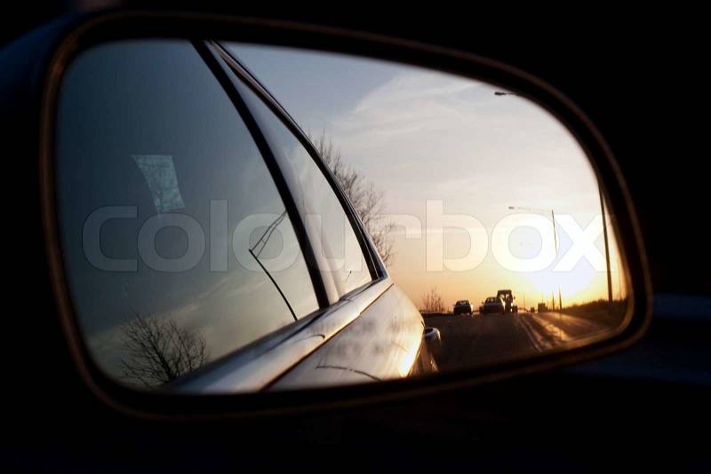View of the sunset from the side view mirror of a car while driving down the roadShallow depth of field, stock photo