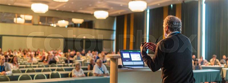 Casualy dressed senior professor giving talk at scientific conference. Audience at the conference hall. Research experts and entrepreneurship event, stock photo