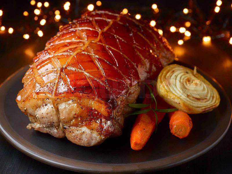 Roasted pork and vegetables on Christmas lights background, stock photo