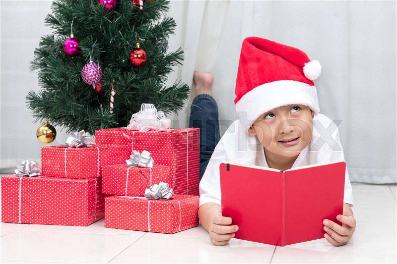 Happy Asian Chinese little boy reading book beside Christmas presents in the living room at home, stock photo