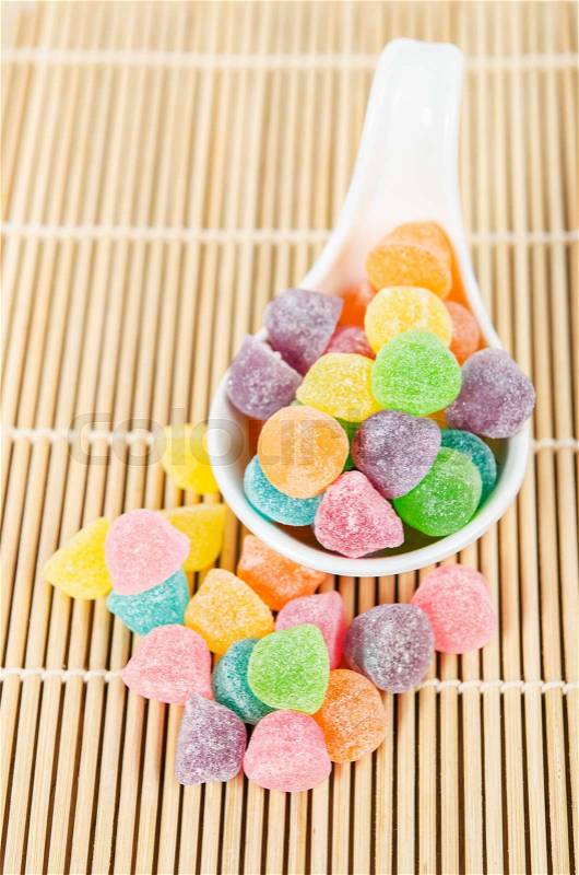 Colorful candies, jelly sugar in white spoon on bamboo mat, stock photo