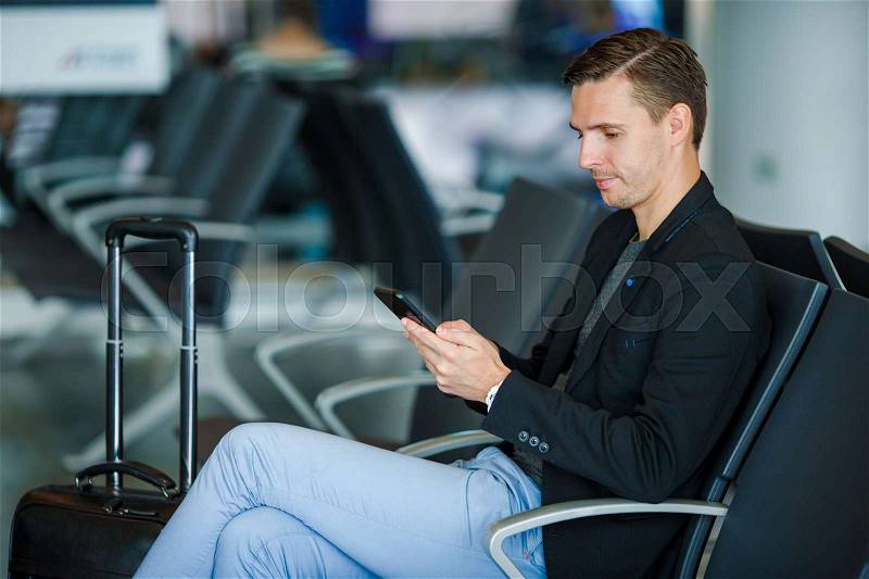 Young man with cellphone inside in airport. Young man with smartphone at the airport while waiting for boarding, stock photo