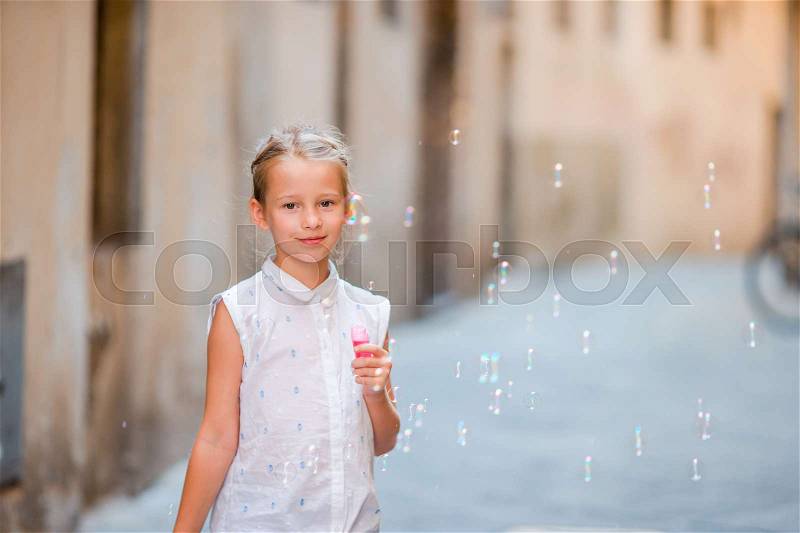 Little girl blowing soap bubbles in european city. Portrait of caucasian kid enjoy summer vacation in Italy, stock photo