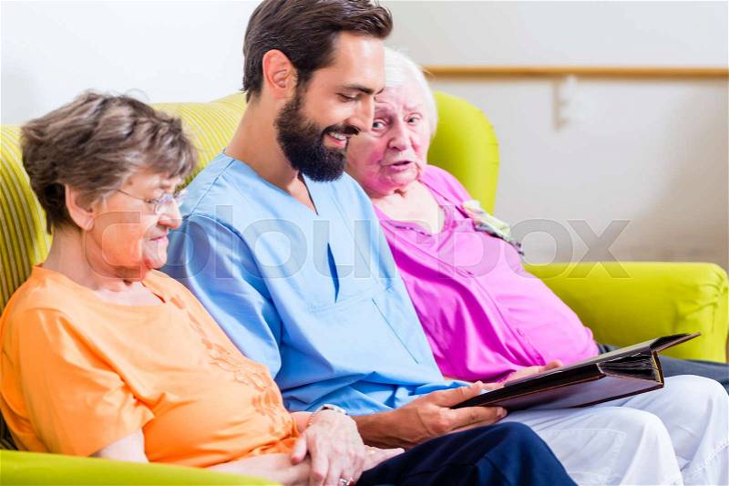 Geriatric nurse looking at pictures with seniors in nursery home, stock photo