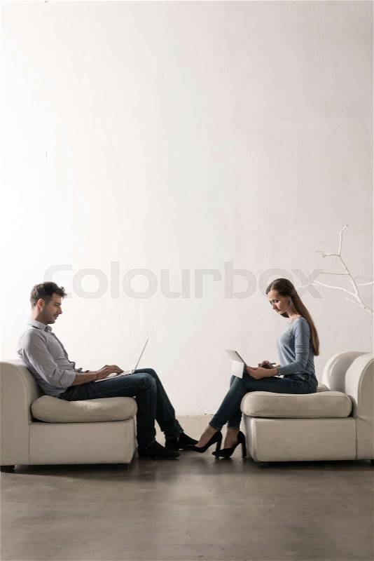 Man and woman sitting in white room face-to-face working, stock photo