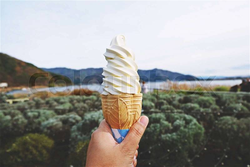 Hand holding vanilla soft ice cream with mountain background, stock photo