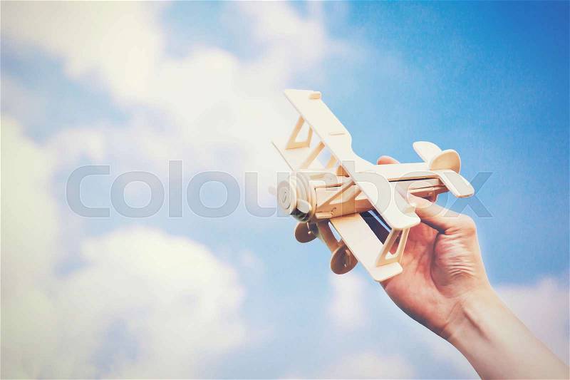 Human hands holding a wooden plane toy over blue sky with copyspace, stock photo