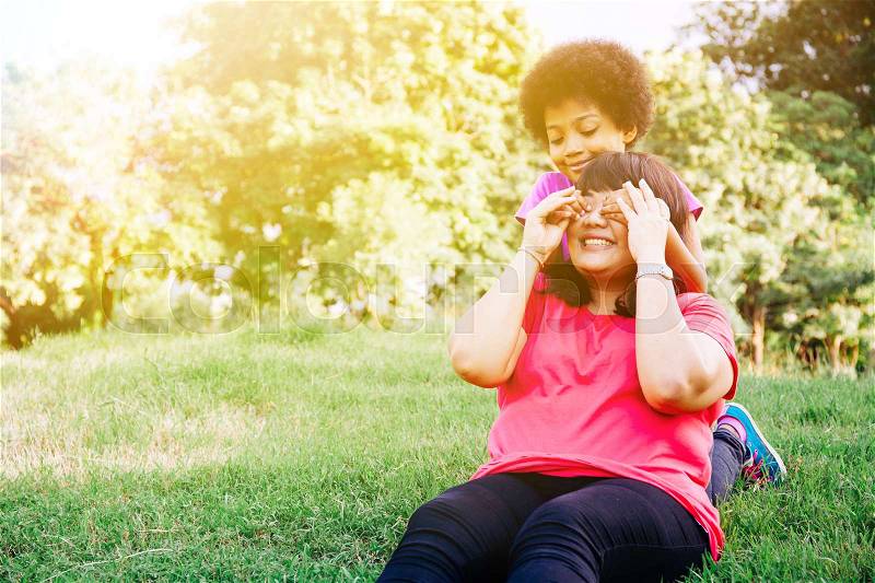 Kid covering mother's eyes in the green park with copy space - Daughter and mother relationship, stock photo