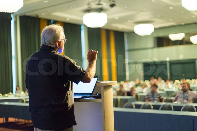 Casualy dressed senior professor giving talk at scientific conference. Audience at the conference hall. Research experts and entrepreneurship event, stock photo