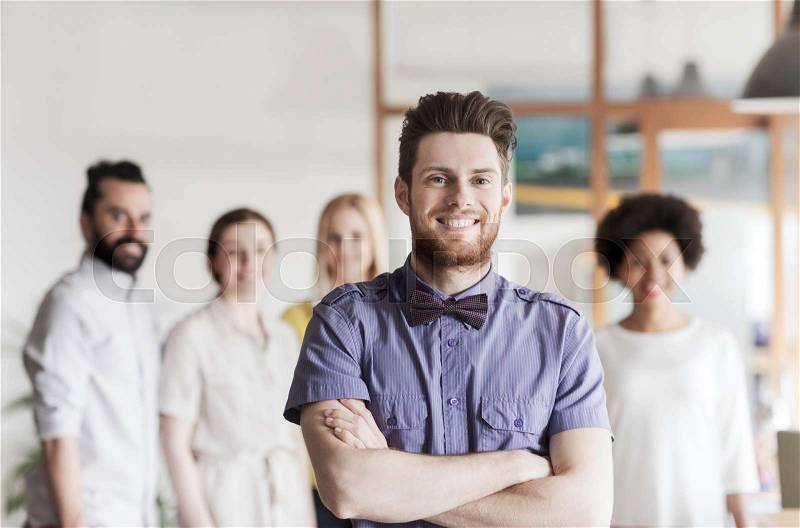 Business, startup, people and teamwork concept - happy young man with beard and bow tie over creative team in office, stock photo