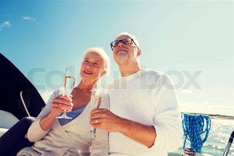 Sailing, age, travel, holidays and people concept - happy senior couple with champagne glasses on sail boat or yacht deck floating in sea, stock photo