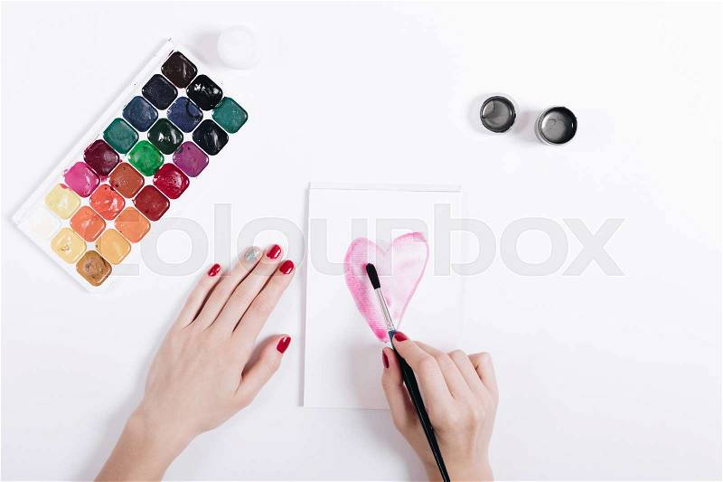 Female hands with red nail polish painted watercolor heart in a notebook, top view, stock photo