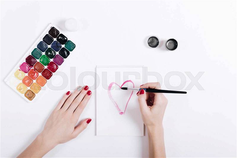 Women\'s hands with red manicure painted watercolor heart in a notebook, top view, stock photo