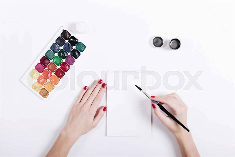Women\'s hands with red nail polish painted watercolors in a notebook, top view, stock photo