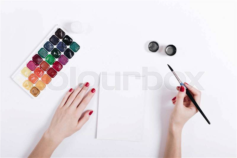 Female hands with red nail polish painted watercolors in a notebook, top view, stock photo