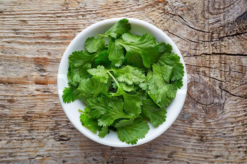 Bowl of coriander leaves on wooden background, top view, stock photo