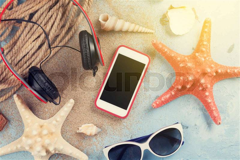 Travel vacation items on stone background. Smartphone, headphones and sunglasses. Top view. Sunny toned, stock photo