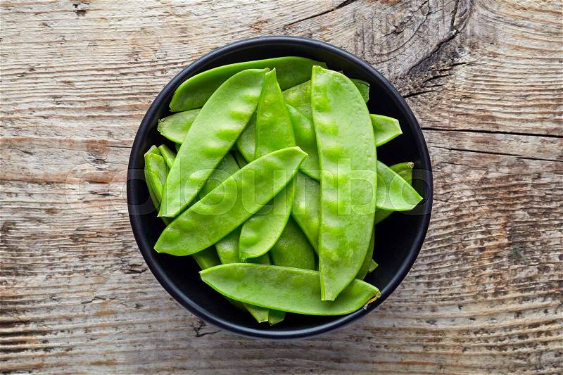 Bowl of snow peas on wooden background, top view, stock photo