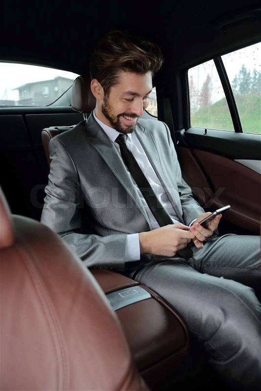 Handsone successful businessman using mobile phone in back seat of car, stock photo