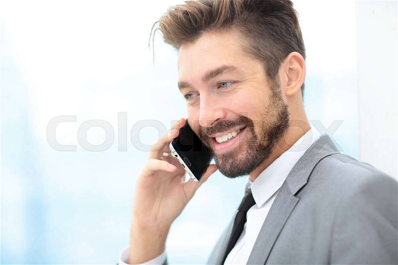 Handsome smiling business man in an office using smartphone, stock photo