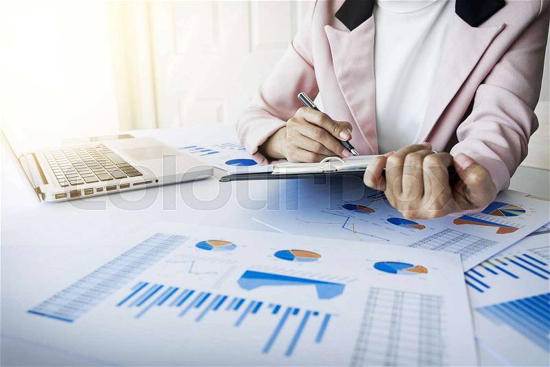Portrait of business woman with laptop, finance graph and writes on a document at her office, stock photo
