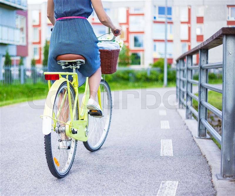 Back view of woman in dress riding vintage bike with wicker basket, stock photo