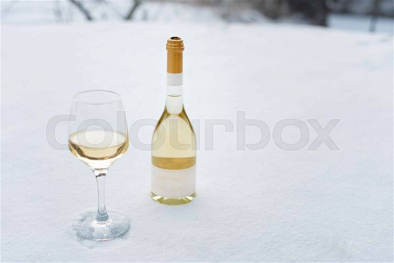 Love, romance, winter holidays, New Year celebration concept. Bottle and glass of white wine chilled by snow, stock photo