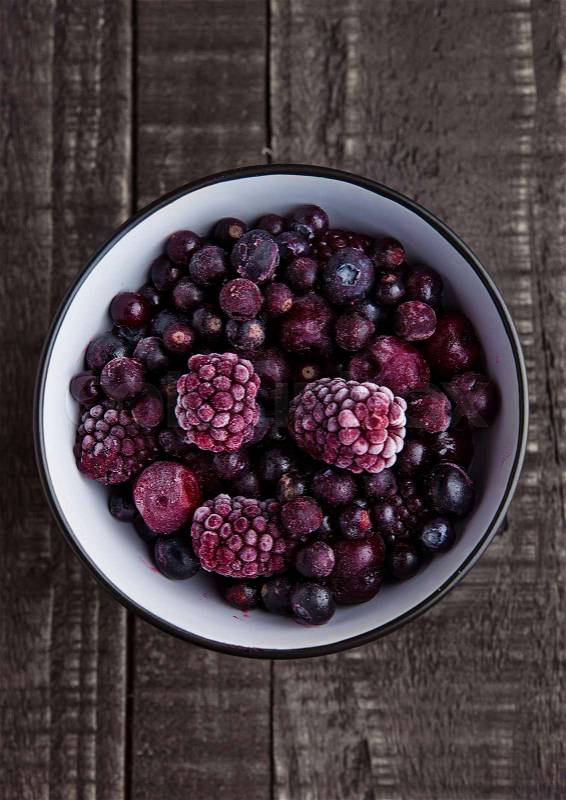 Frozen berries mix in a black bowl on wooden background. Still life photography, stock photo