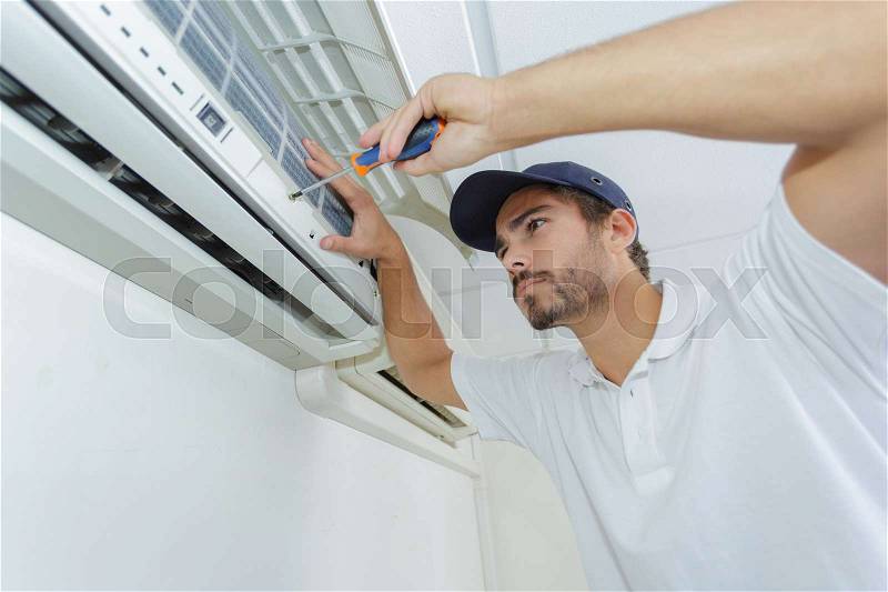 Portrait of mid-adult male technician repairing air conditioner, stock photo