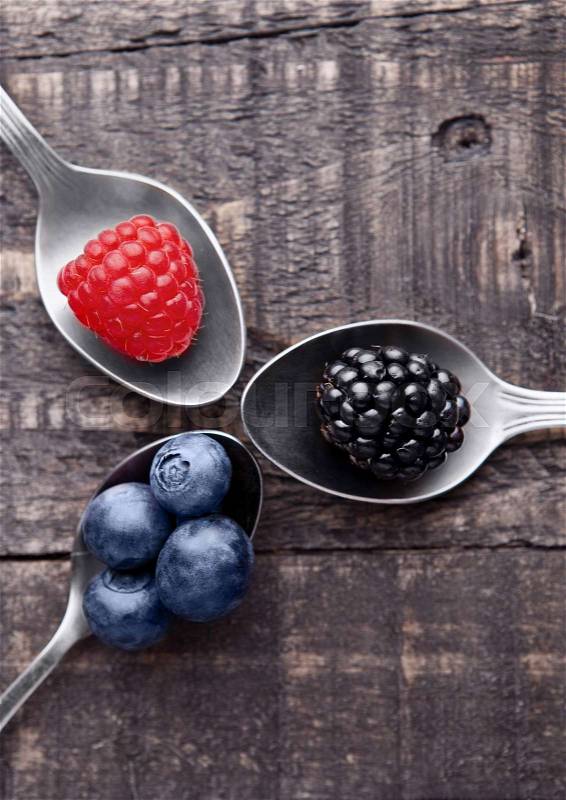 Raspberry blueberry and blackberry on spoon and wooden table. Still life photography, stock photo