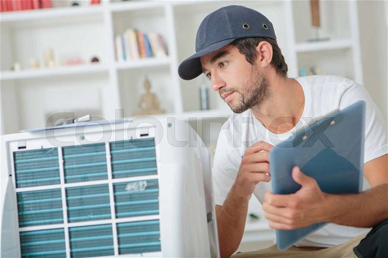 Handsome technician checking the ac at clients home, stock photo