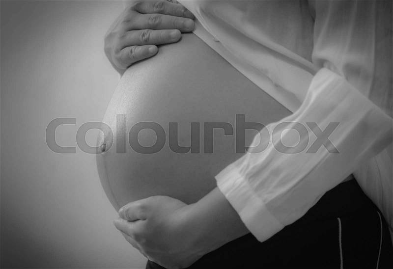 Black and white image of a pregnant woman touching her belly with hands, stock photo