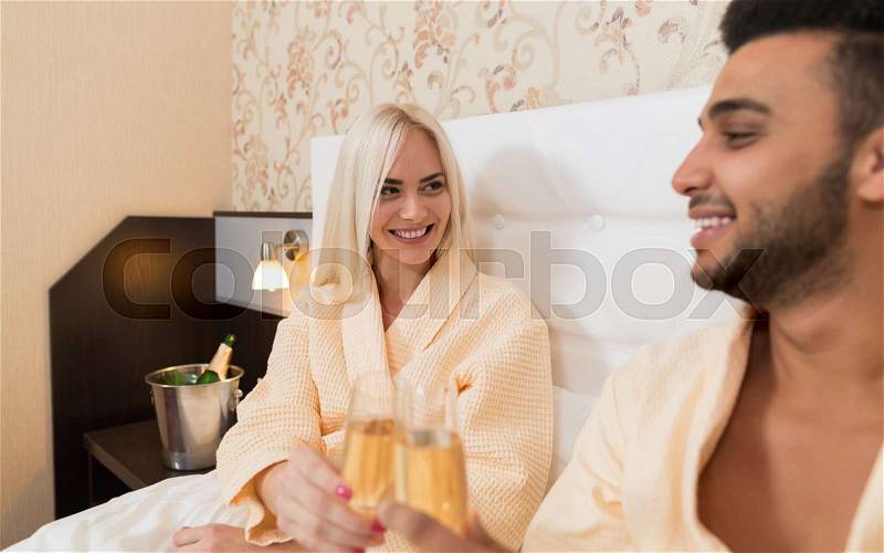 Young Couple Lying In Hotel Bed Drink Champange, Happy Smile Hispanic Man And Woman Lovers In Bedroom, stock photo