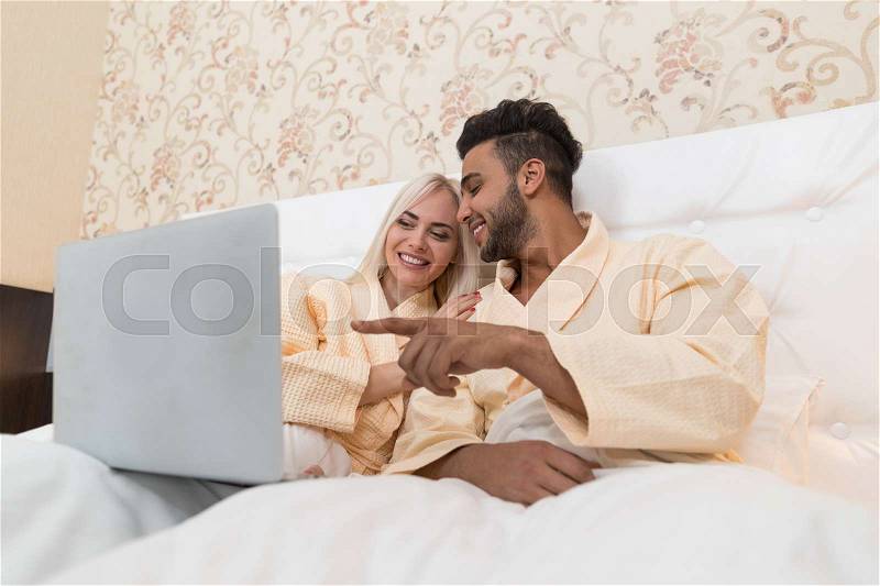 Young Couple Lying In Hotel Bed, Happy Smile Hispanic Man And Woman Using Laptop Computer, Lovers In Bedroom, stock photo