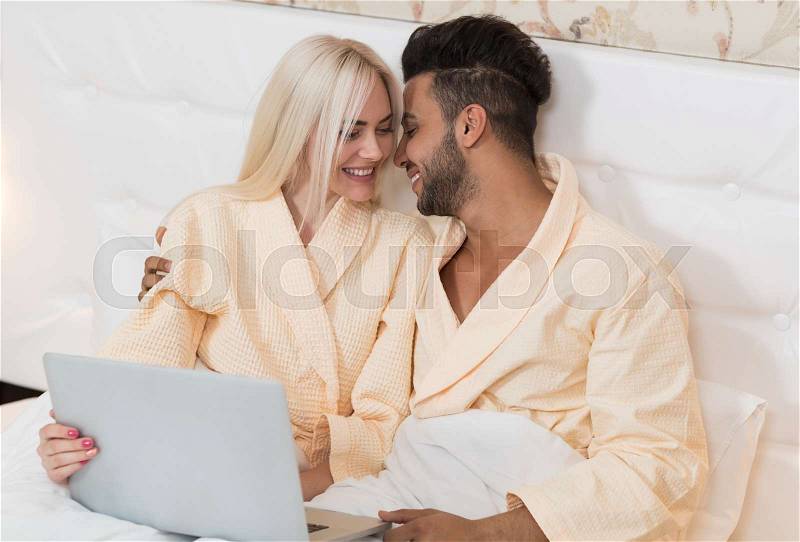 Young Couple Lying In Hotel Bed, Happy Smile Hispanic Man And Woman Using Laptop Computer, Lovers In Bedroom, stock photo