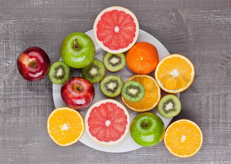 Fruits mix grapefruit orange and kiwi on the plate on wooden background, stock photo