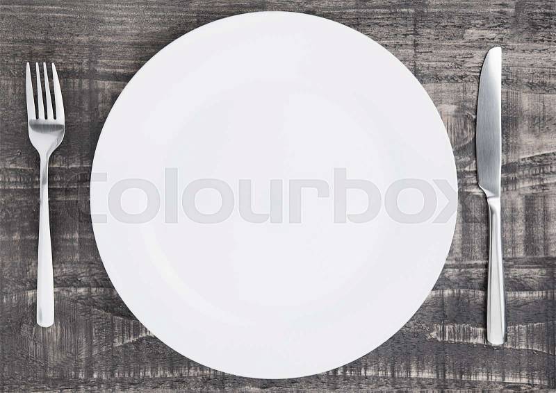 White round plate with fork and knife on wooden board background, stock photo