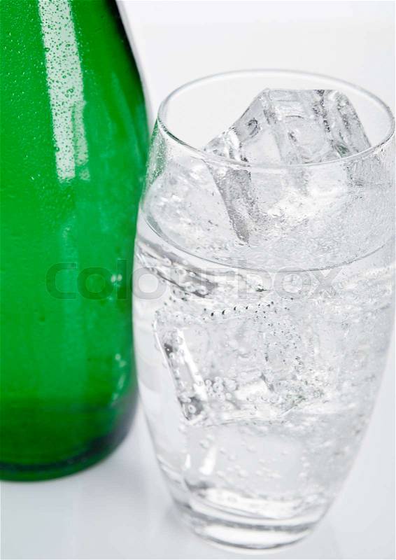 Bottle and glass with healthy sparkling water with ice cubes on white, stock photo