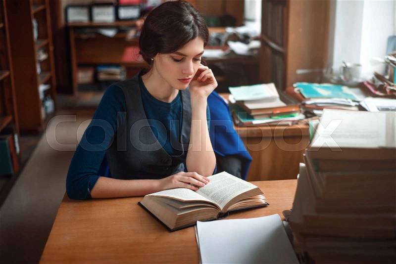 Portrait of clever student reading a book in university library, stock photo