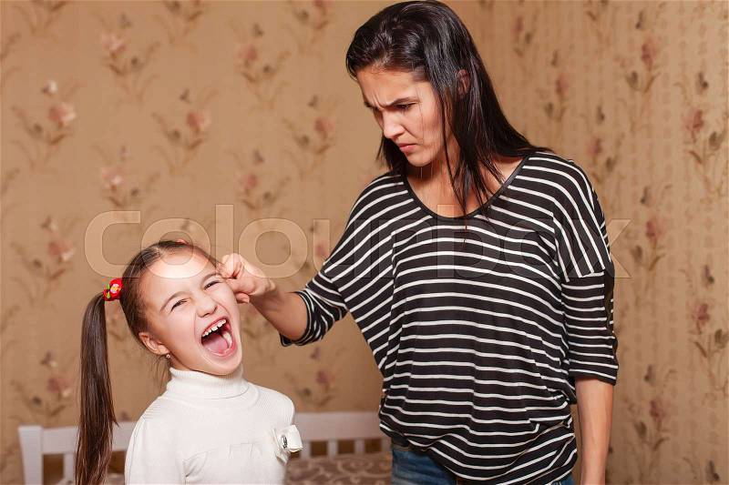 Strict mother holds the little daughter by an ear. Child education concept, stock photo